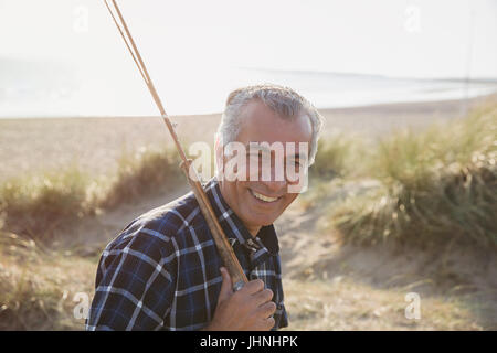 Portrait of smiling senior homme avec la canne à pêche marche sur sunny beach Banque D'Images