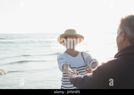 Playful young couple holding hands on beach océan ensoleillé Banque D'Images