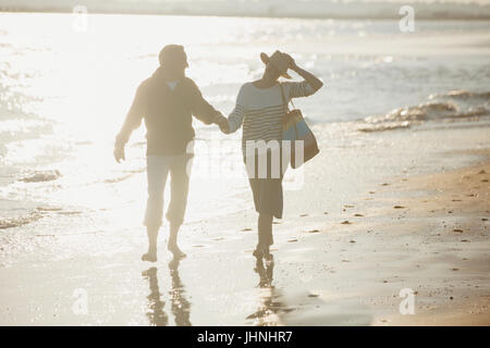 Young couple holding hands and walking on sunny beach Banque D'Images