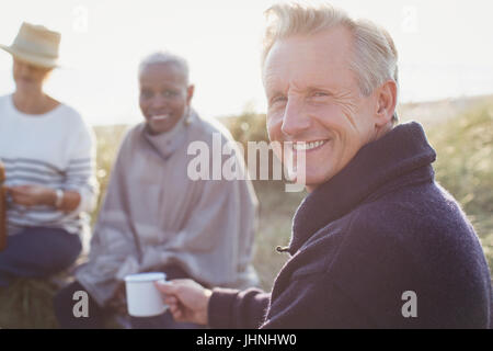 Portrait of smiling senior man drinking coffee avec des amis sur sunny beach Banque D'Images