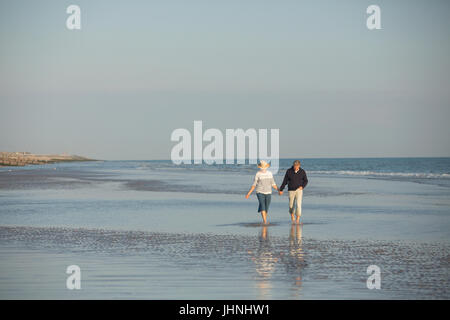 Young couple holding hands walking in sunny beach surf océan Banque D'Images