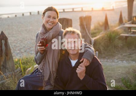 Portrait of smiling young couple holding hands et boire du vin sur sunset beach Banque D'Images