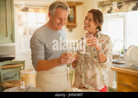 Smiling mature couple drinking wine and cooking in kitchen Banque D'Images