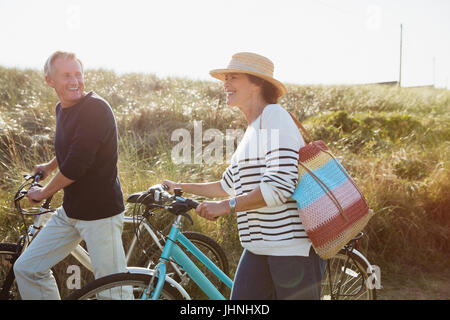 Mature couple walking des vélos sur le chemin de l'herbe de sunny beach Banque D'Images