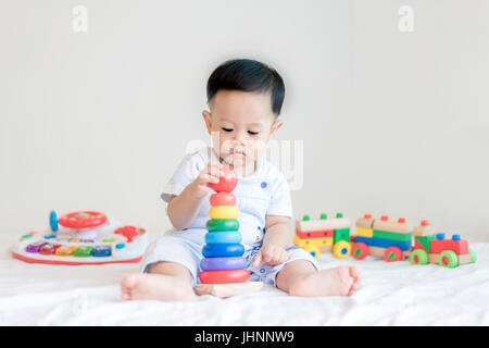 Adorable Bébé Garçon 9 mois asiatique assis sur le lit et jouer avec les jouets de couleur à la maison. Banque D'Images