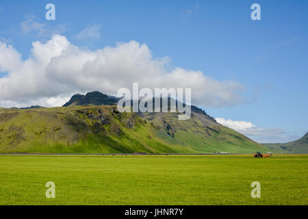 Près de la montagne de volcan Eyjafjallajokull en Islande. Champ vert, bleu ciel, journée ensoleillée et du tracteur dans l'arrière-plan. Banque D'Images