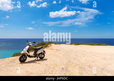 Vieux scooter garé sur la belle côte avec vue sur la mer sur l'île de Milos, Cyclades, en Grèce. Banque D'Images