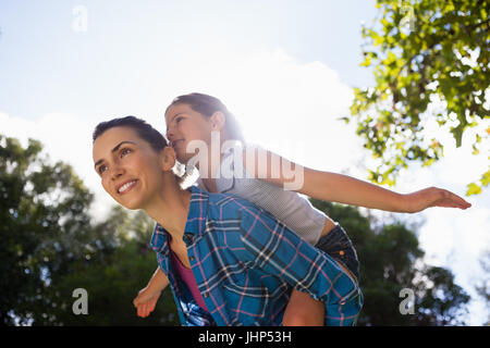 Low angle view of Girl with arms outstretched appréciant piggyback ride on mère contre sky in backyard Banque D'Images