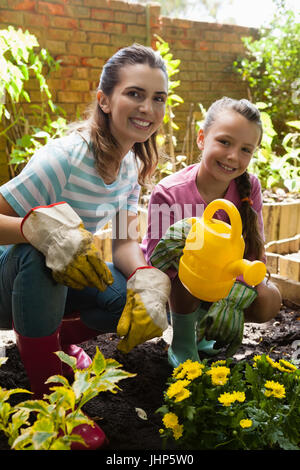 Portrait de femme et fille accroupie de fleurs avec arrière-cour à l'arrosoir Banque D'Images