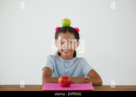 Portrait de lycéenne assis avec green apple sur sa tête contre fond blanc Banque D'Images