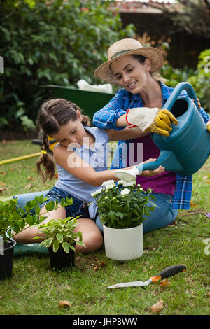 Fille mère aidant dans l'arrosage des plantes en pot sur terrain à jardin Banque D'Images