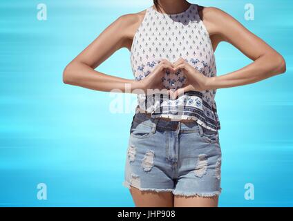 Digital composite de femme millénaire mid section faire coeur avec les mains contre floue fond bleu Banque D'Images