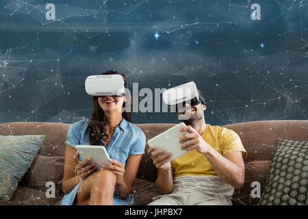 Digital composite de l'heureux couple en VR headsets assis contre l'arrière-plan galaxy Banque D'Images