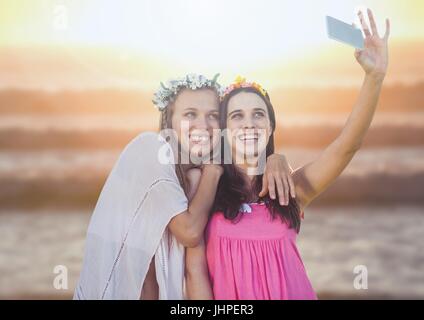 Composite numérique des femmes prenant selfies occasionnels photo devant le coucher du soleil sur la mer Banque D'Images