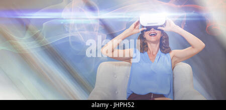 Femme heureuse en utilisant des lunettes de réalité virtuelle tout en étant assis sur le canapé contre low angle view of glass ceiling in office Banque D'Images