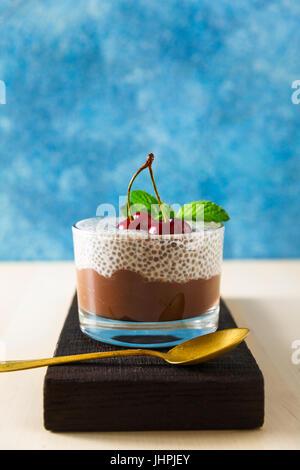 Dessert d'été : à partir de deux couches de mousse au chocolat et de pudding de chia dans une tasse en verre sur une planche en bois , sur un fond bleu. Avec de cherri Banque D'Images