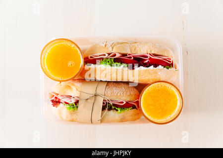 Sandwich avec pain frais, avec du jambon et des tomates, laitue. dans une boîte à lunch. Et deux verres de jus d'orange fraîchement pressé, copy space Banque D'Images