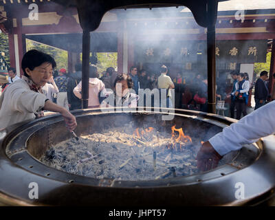 Femme japonaise lights bâton d'encens dans le grand brûleur d'encens en bronze ou koro au temple Senso-ji. 15 avril 2014 - Asakusa, Tokyo, Japon Banque D'Images