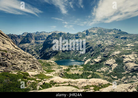 Vue plongeante sur le lac de Melo à la tête de la vallée de la Restonica près de Corte en Corse avec des rochers en premier plan et le ciel bleu Banque D'Images