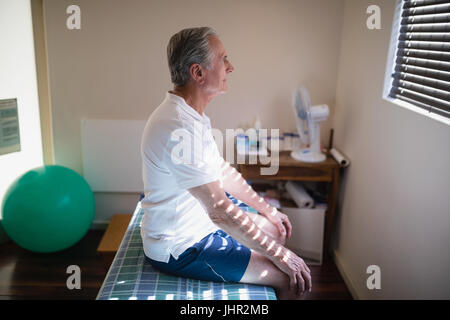 Vue latérale du senior male patient sitting on bed at Hospital ward Banque D'Images