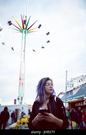 Thoughtful woman using mobile phone in amusement park Banque D'Images