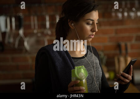 Close up of woman using phone tout en ayant un verre dans la cuisine à la maison Banque D'Images