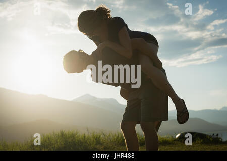 Man giving piggyback ride à son partenaire en campagne au crépuscule Banque D'Images