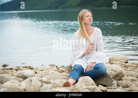 Belle jeune femme assise sur des rochers contre lake Banque D'Images