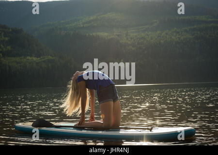 Vue de côté femme pratiquant sur Ustrasana paddleboard dans le lac contre mountain Banque D'Images