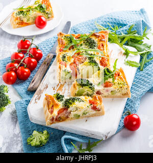 Maison végétariens délicieux gâteau, quiche aux tomates cerise tranchées, de brocoli et de fromage blanc aux herbes sur la vieille planche à découper. Concept d'aliments sains. Banque D'Images