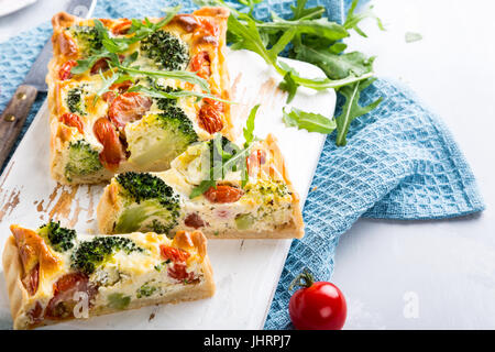 Maison végétariens délicieux gâteau, quiche aux tomates cerise tranchées, de brocoli et de fromage blanc aux herbes sur la vieille planche à découper. Concept d'aliments sains. Banque D'Images