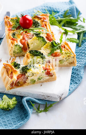 Maison végétariens délicieux gâteau, quiche aux tomates cerise tranchées, de brocoli et de fromage blanc aux herbes sur la vieille planche à découper. Concept d'aliments sains. Banque D'Images