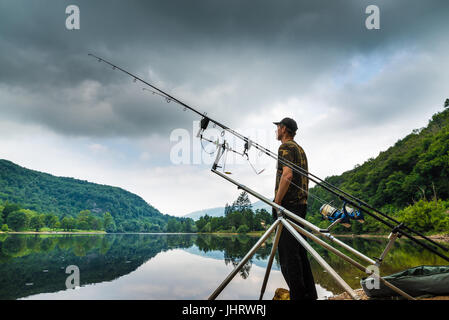 Aventures de pêche, pêche à la carpe. Pêcheur sur la rive d'un lac dans un matin avec ciel sombre et des nuages gris Banque D'Images