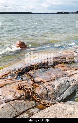 Les vagues de l'eau mousseuse blanc frappé en rocky seashore. Vieux fer rouillé sur les roches de la chaîne. Banque D'Images