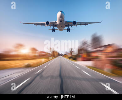 Avion de passagers avec effet de flou. Avion vole dans le ciel au coucher du soleil sur le rural route asphaltée au coucher du soleil en Pays-Bas. Airplan Landing Banque D'Images