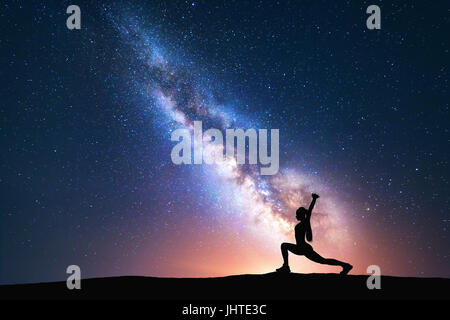 Voie Lactée avec silhouette d'une femme pratiquant le yoga sur le terrain. Beau paysage et méditant girl contre nuit ciel étoilé avec bri Banque D'Images