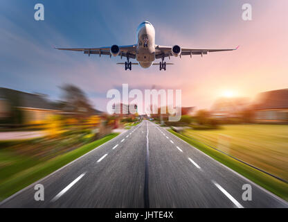 Avion de passagers avec effet de flou. Avion vole dans le ciel au coucher du soleil sur le rural route asphaltée au coucher du soleil en Pays-Bas. Airplan Landing Banque D'Images