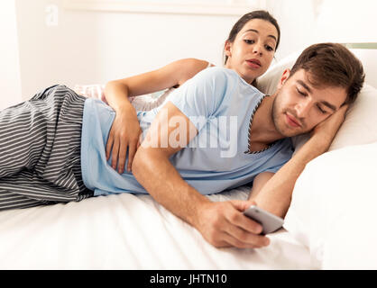 Addicted jeune homme sur le lit texter en femme a l'air en colère Banque D'Images