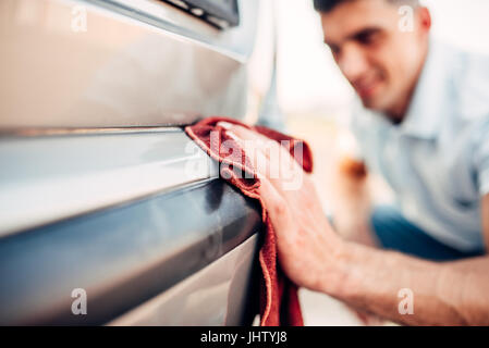 Polissage extérieur voiture sur la station de lavage. L'homme frotte pare-choc du véhicule automobile avec polish Banque D'Images