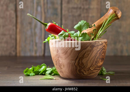 Différentes herbes sur une vieille table en bois . Mortier en bois avec le romarin, la coriandre, le thym et le persil. Banque D'Images