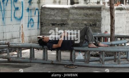 L'homme de dormir sur un banc du Parc de la ville espace ouvert à Sathorn/de la station de métro aérien BTS Saphan Taksin Bangkok Thaïlande Banque D'Images