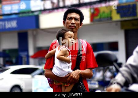 ANTIPOLO CITY, PHILIPPINES - le 13 juillet 2017 : un père porte son enfant tout en marchant dans la rue. Banque D'Images