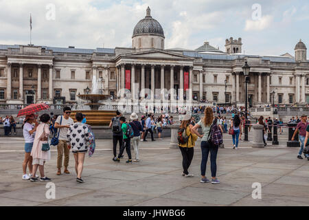 Les touristes et les habitants debout et assis à l'extérieur de la galerie sur Trafalgar Square, Londres, se détendre, discuter, la vérification directe, en tenant photographe Banque D'Images