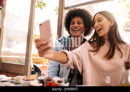 Jeune couple assis dans le café et en tenant avec selfies téléphone intelligent. Beautiful woman taking self portrait avec son petit ami dans un restaurant. Banque D'Images