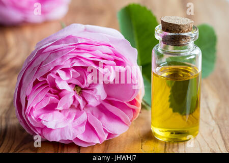 Une bouteille d'huile essentielle avec une fleur rose sur un fond de bois Banque D'Images