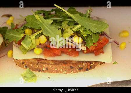 La préparation des aliments avec un morceau de pain multigrains, tranche de mozzarella, salade, tomates et maïs Banque D'Images