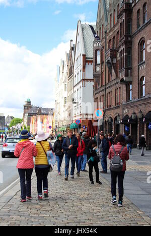 Les touristes d'explorer le site historique de Bryggen, Bergen, avec des tenues rose et jaune pour correspondre à l'avant des bâtiments en bois Banque D'Images