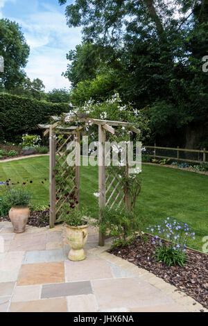 Une arche de jardin Couverte de jasmin (Jasminum officinale) entre un patio en pierre et de pelouse, avec des pots de cosmos chocolat Cosmos atrosanguineus (au) Banque D'Images