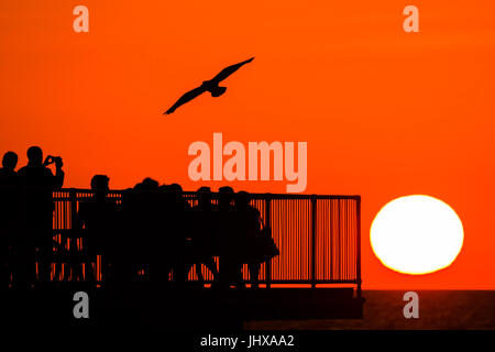 Aberystwyth, Pays de Galles, Royaume-Uni. 16 juillet, 2017. Météo France : des gens assis sur la fin d'Aberystwyth's Victorian station pier, silhouetté au coucher du soleil dans un ciel orange flamboyant sur la baie de Cardigan sur la côte ouest du pays de Galles Crédit photo : Keith Morris/Alamy Live News Banque D'Images