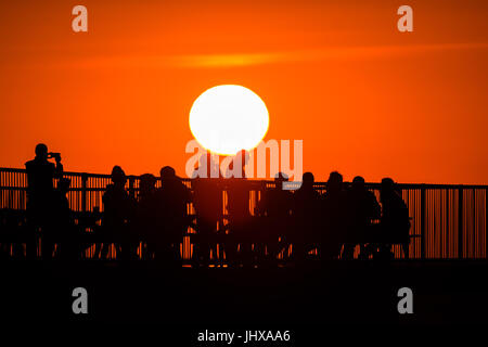 Aberystwyth, Pays de Galles, Royaume-Uni. 16 juillet, 2017. Météo France : des gens assis sur la fin d'Aberystwyth's Victorian station pier, silhouetté au coucher du soleil dans un ciel orange flamboyant sur la baie de Cardigan sur la côte ouest du pays de Galles Crédit photo : Keith Morris/Alamy Live News Banque D'Images